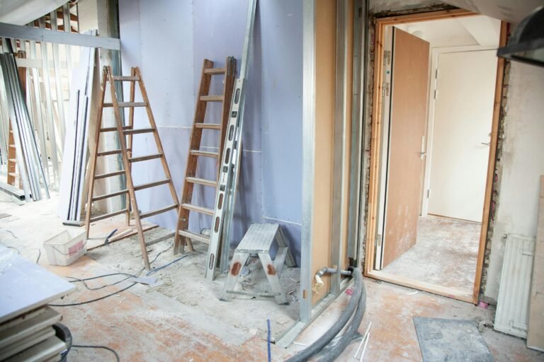 a hallway with broken down walls, ladders and step stools stood up, and an open door leading away from the remodel site