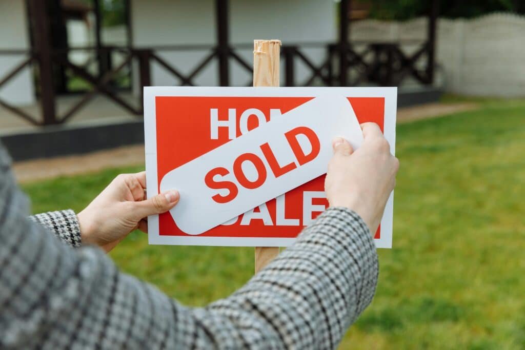 close up of a realtor sticking on a 'sold' sticker over a wooden for sale sign